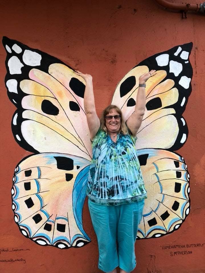 Dr. Colleen Snyder standing with her arms raised in front of a painted butterfly mural, so the wings appear to be hers.