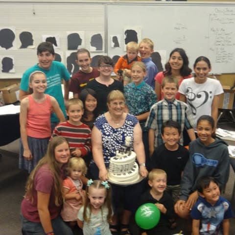 About twenty students crowded around their teacher, who is holding a cake iced to look like a piano keyboard.